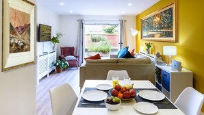 Una sala de estar moderna con comedor, que incluye un sofá, una mesa de comedor con platos y fruta, y un cuadro grande en la pared.