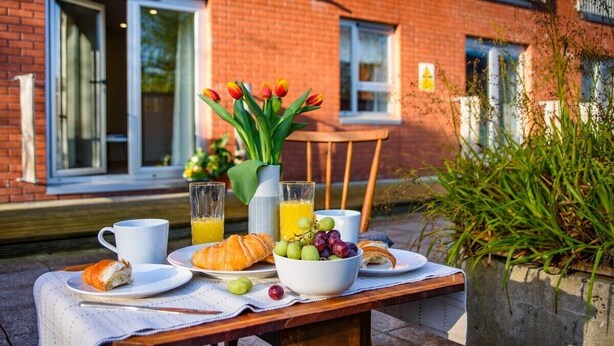 Un desayuno preparado en una mesa al aire libre, con un edificio de ladrillo al fondo.