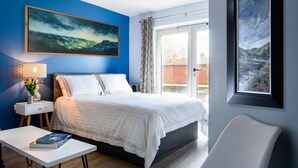 Un dormitorio moderno con cama, mesita de noche con lámpara, una silla y vistas al exterior a través de una ventana.