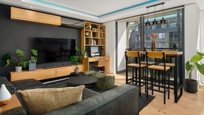 Ein modernes Wohnzimmer mit Flachbildfernseher, Holzregalen, einer Essecke mit Stühlen und Topfpflanzen.