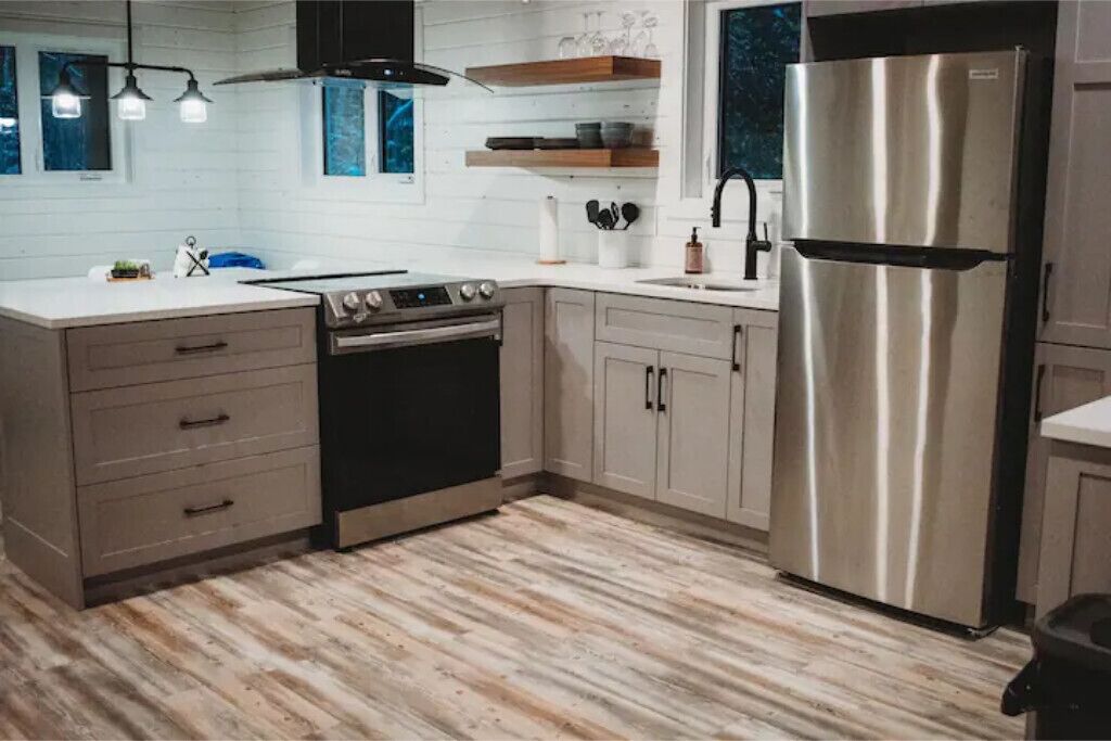 A modern kitchen with a stainless steel refrigerator, a built-in oven, and a gas stove. There are wooden cabinets and a countertop with a sink.