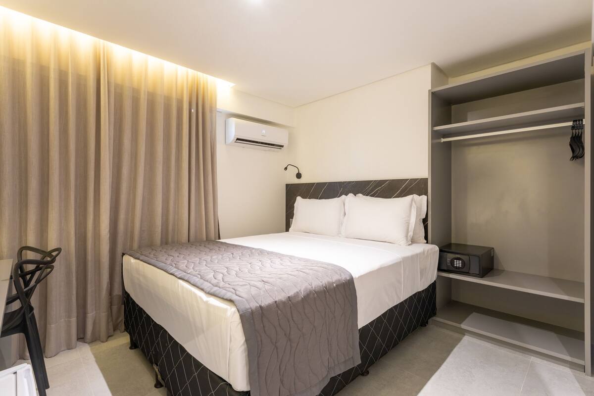 Habitación de hotel con cama, escritorio, armario y aire acondicionado.