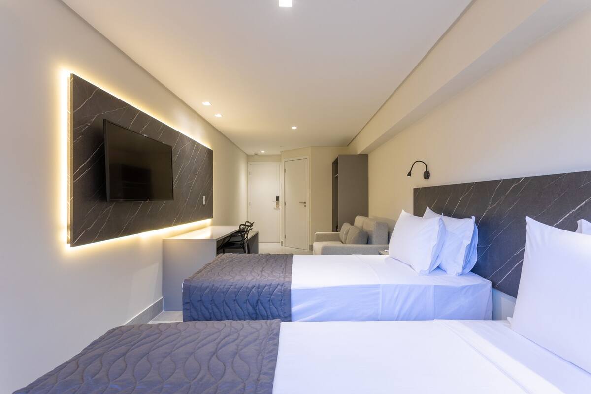 Una habitación de hotel moderna con dos camas, un televisor de pantalla plana en la pared, un escritorio y una zona de estar con un sofá.