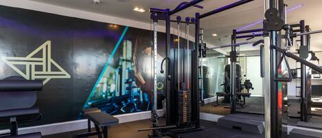 Une salle de sport équipée de matériel d’exercice, dotée d’un grand miroir et d’un mur orné d’un motif géométrique.