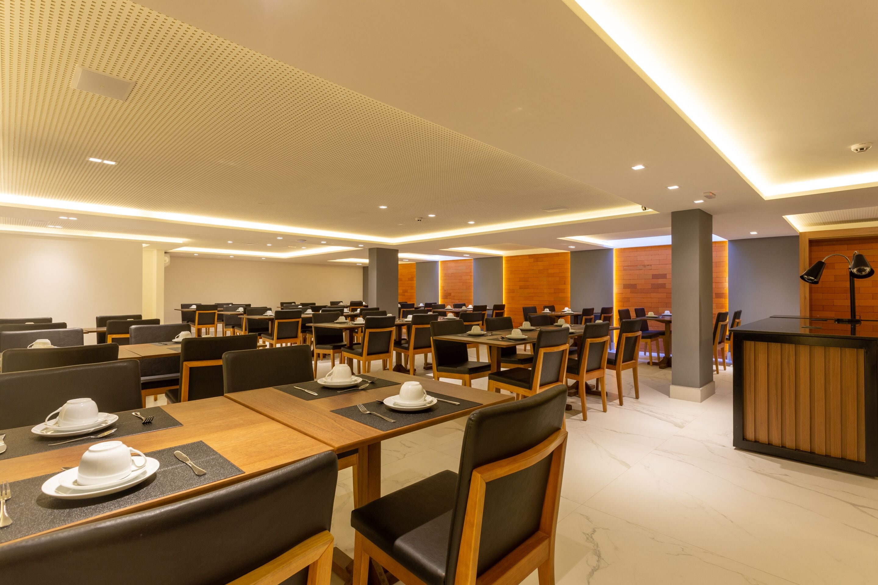 Un vaste espace dédié à la restauration, avec de nombreuses tables et chaises, un comptoir d’accueil et un design moderne au niveau du plafond.
