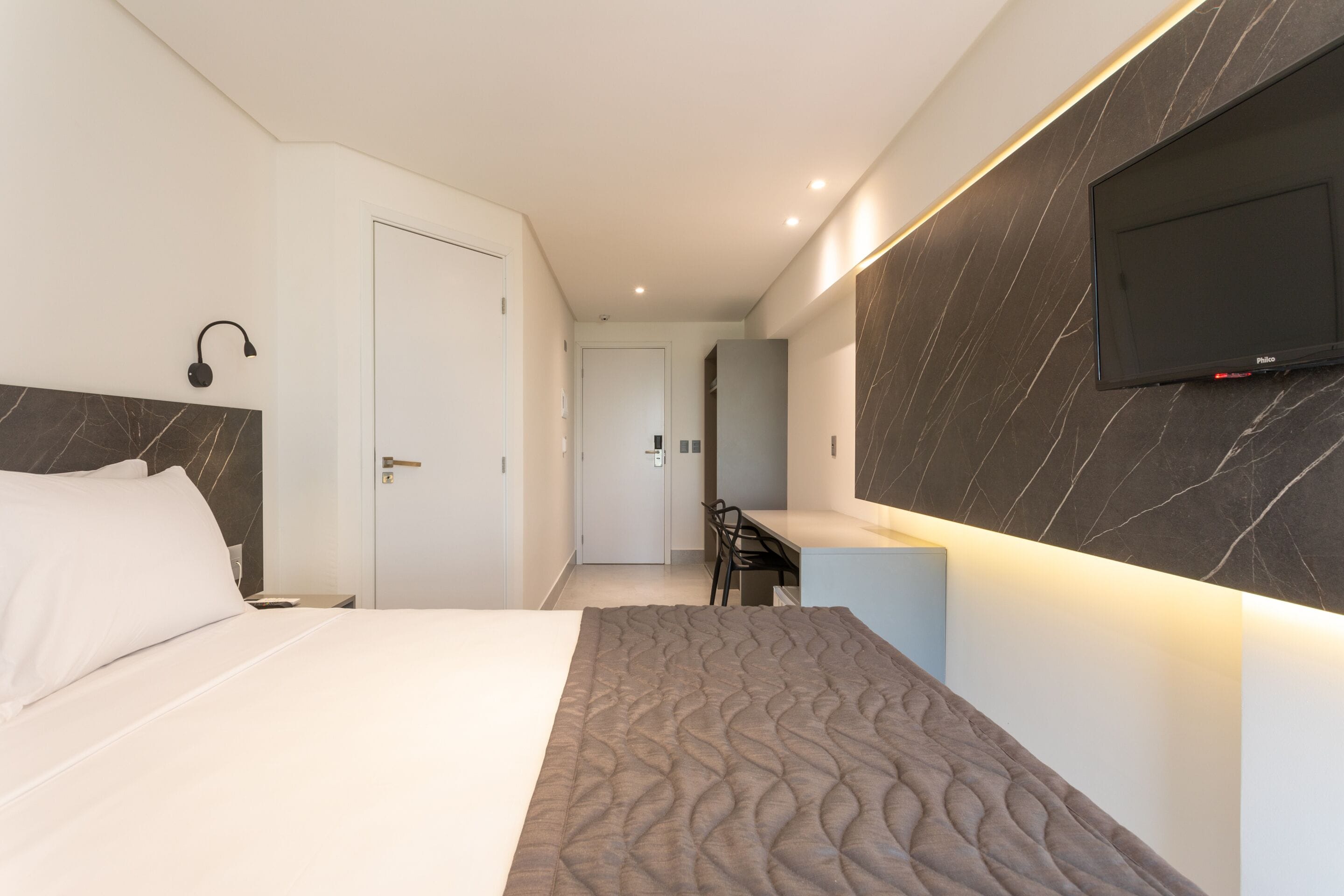 Une chambre d’hôtel moderne, dotée d’un grand lit, d’un bureau et d’un téléviseur à écran plat fixé au mur.
