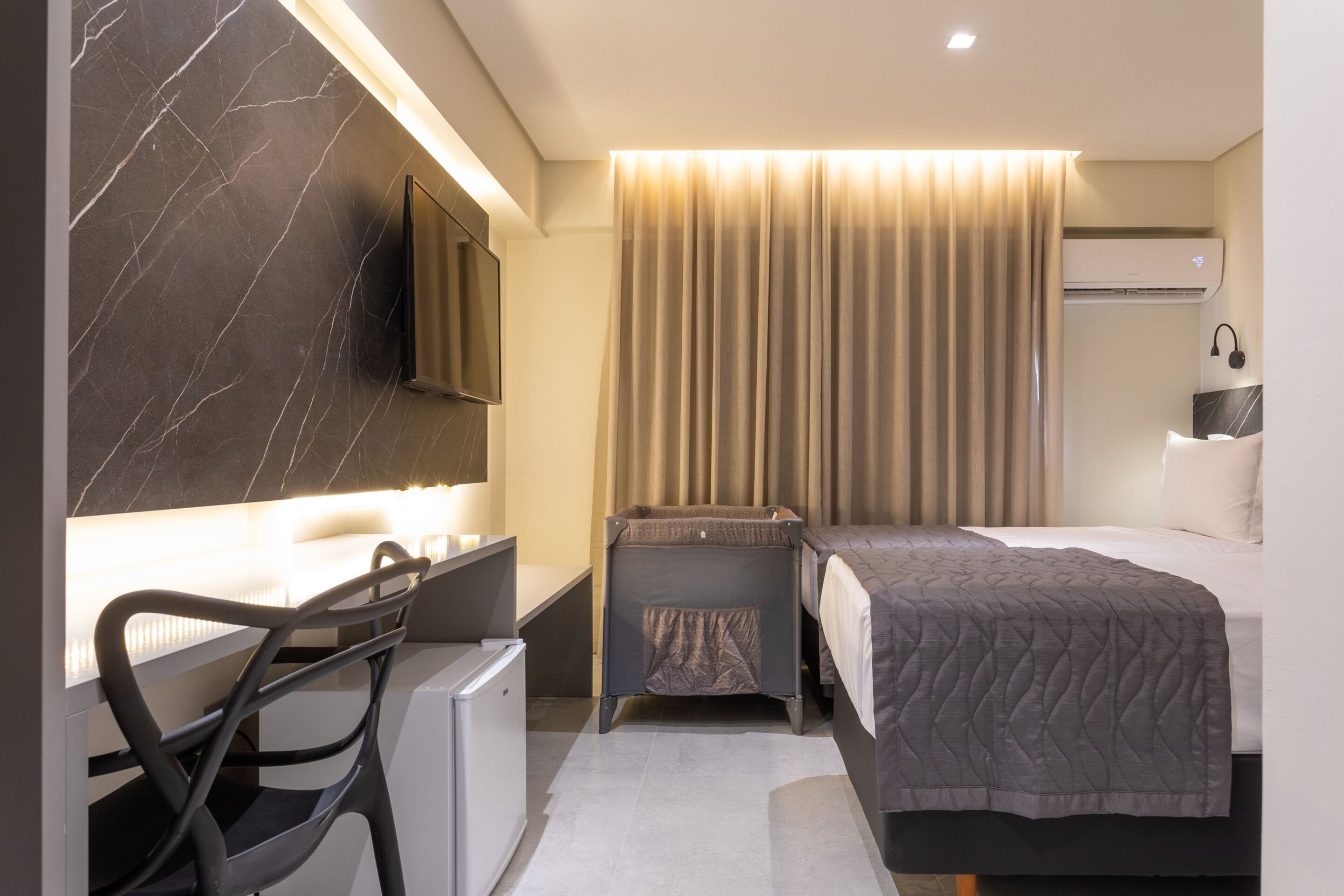 Een moderne hotelkamer met een bureau, stoel, bed en een aan de muur bevestigde televisie.