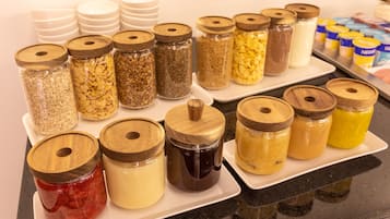 Diversos alimentos em potes com tampas de madeira, dispostos sobre uma bandeja branca.