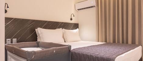 A hotel room with a bed, a small seating area with a screen, an air conditioning unit, and a curtain.