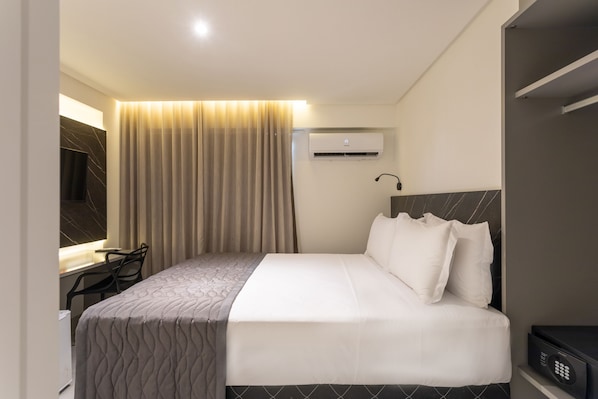 Quarto de hotel com cama, escrivaninha, cadeira, ar condicionado e televisão.