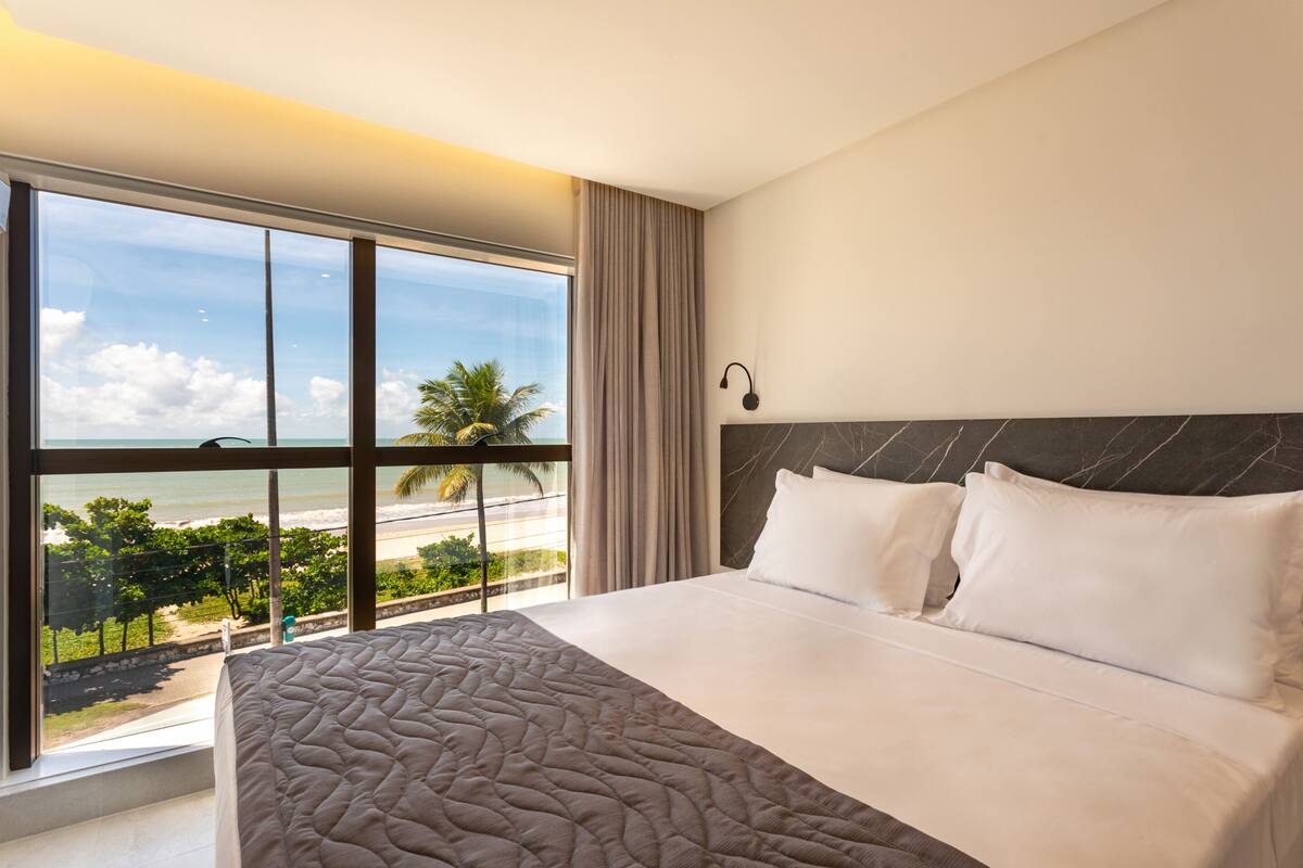 Habitación de hotel con una cama grande, vista a la playa y un diseño moderno.