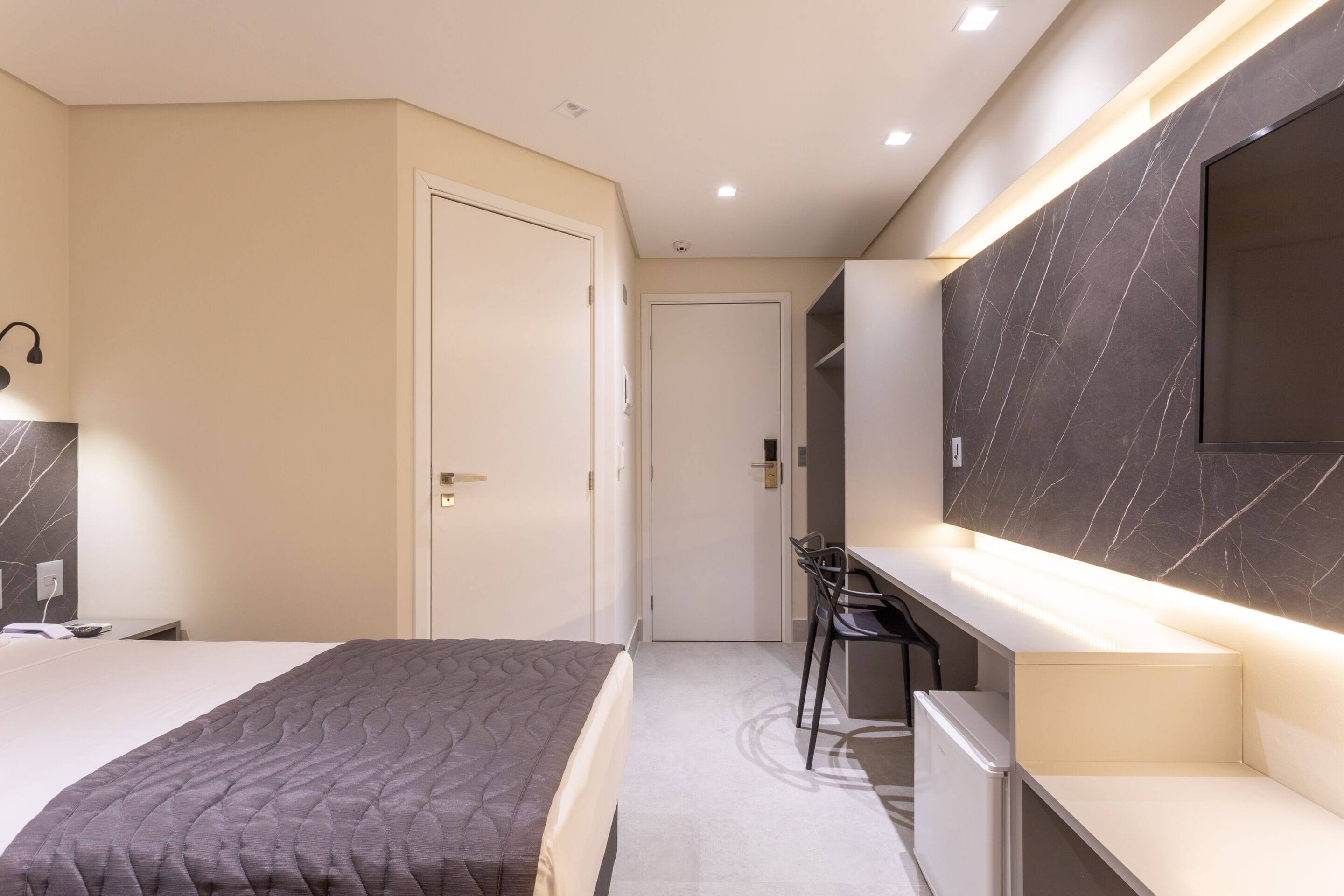 Ein modernes Schlafzimmer mit einem Bett, einem Schreibtisch und einem an der Wand befestigten Fernseher.