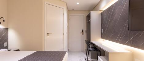 A modern bedroom with a bed, a desk, and a TV mounted on the wall.