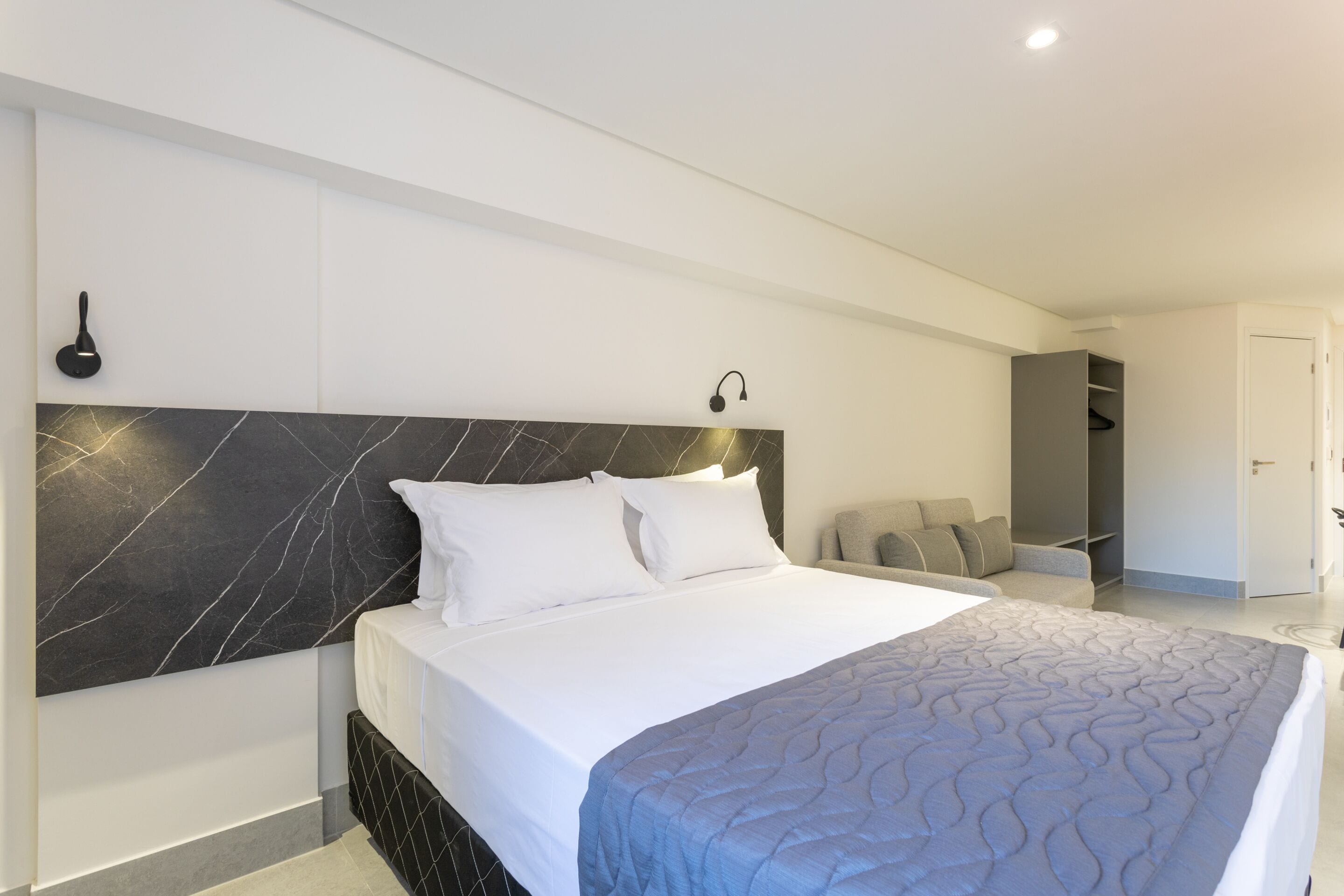 Una habitación de hotel moderna con una cama grande, cabecera de mármol y armario empotrado.