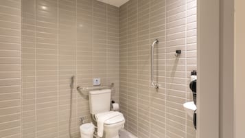 Ein modernes Badezimmer mit beigelfarben gefliesten Wänden, einer weißen Toilette, einer Handbrause und einem Handföhn.