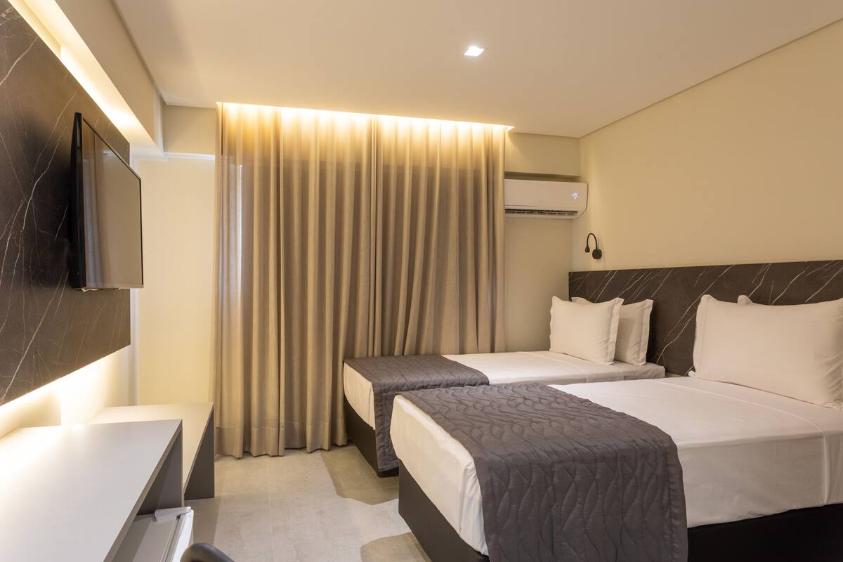 Habitación de hotel con dos camas, un escritorio, un televisor de pantalla plana y un equipo de aire acondicionado.