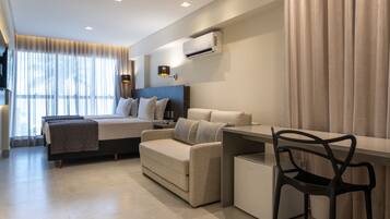 Quarto de hotel moderno com cama, sofá, escrivaninha e uma cadeira.