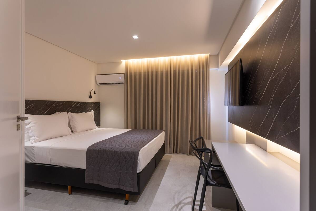 Una habitación de hotel moderna con cama, mesita de noche, silla y televisor en la pared.
