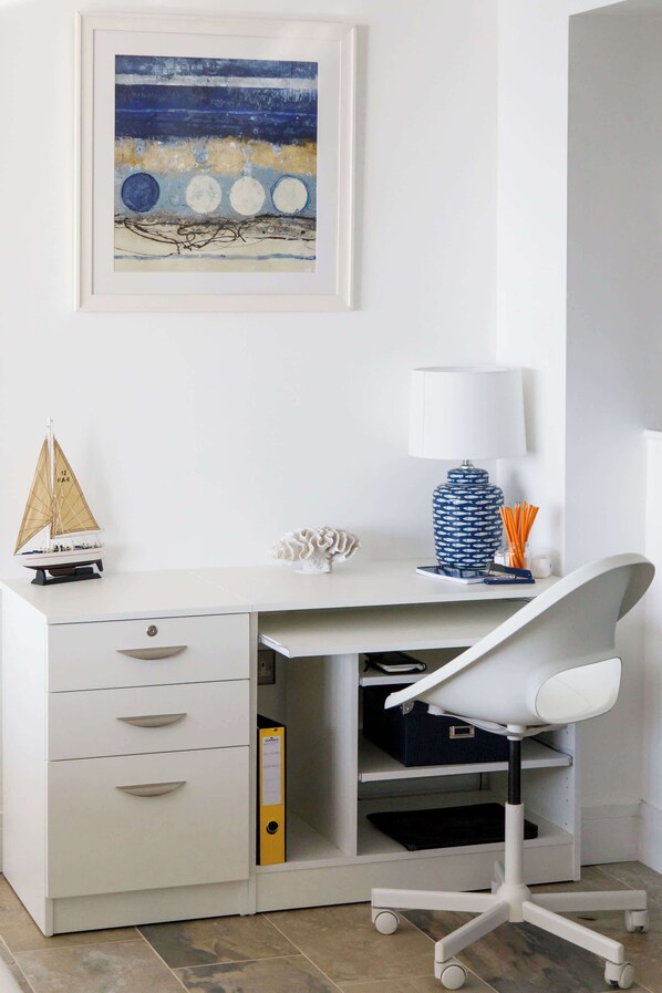 A white desk with a sailboat model, a blue vase, and a white chair.