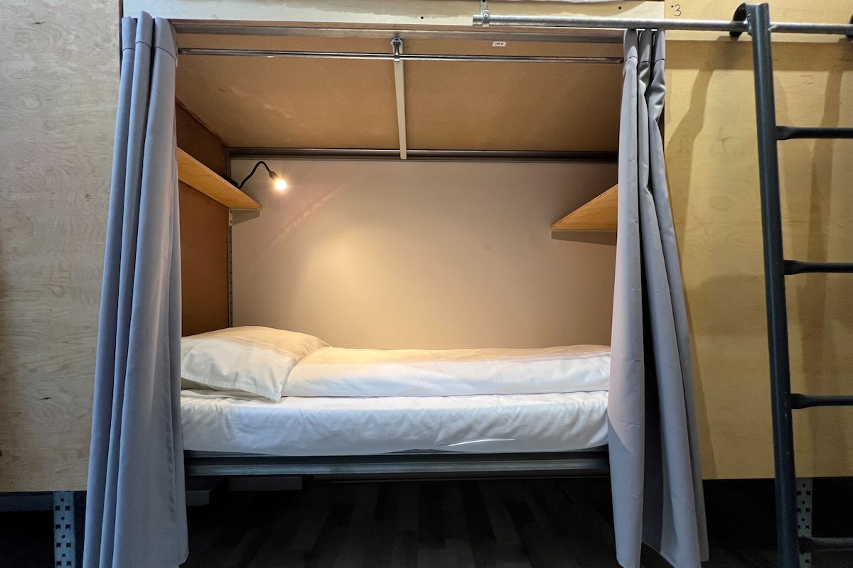 A bunk bed with a headboard, a pull-out desk, and a single bedside lamp.