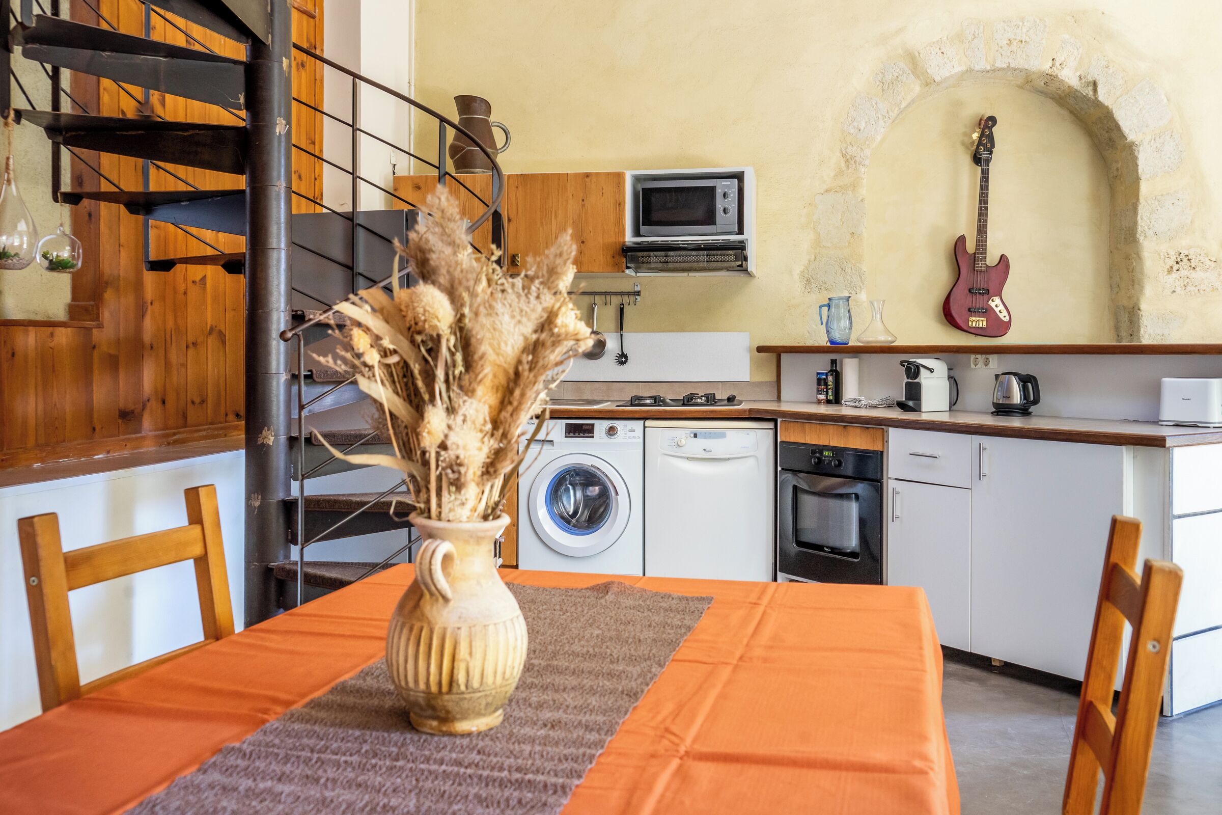 Una cocina equipada con microondas, lavadora, horno y una guitarra.