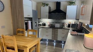 A modern kitchen with white cabinets, a black range hood, and a wooden dining table.