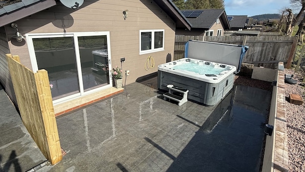 A residential backyard with a hot tub, a covered patio, and a wooden fence.
