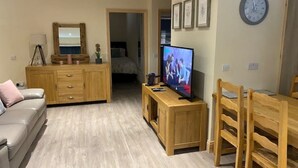 A living room with a wooden TV stand, a sofa, a dining table with chairs, a mirror, and a clock on the wall.