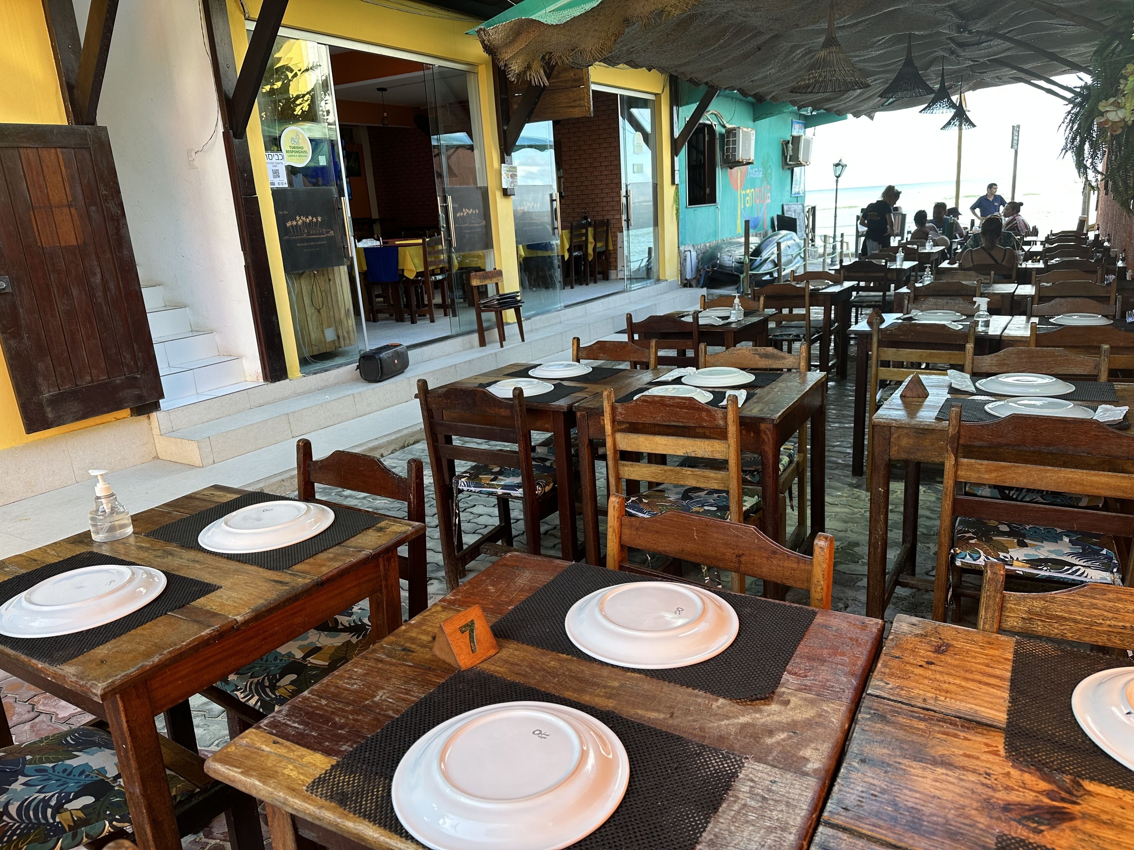 An outdoor restaurant with wooden tables and chairs, some with placemats and plates.