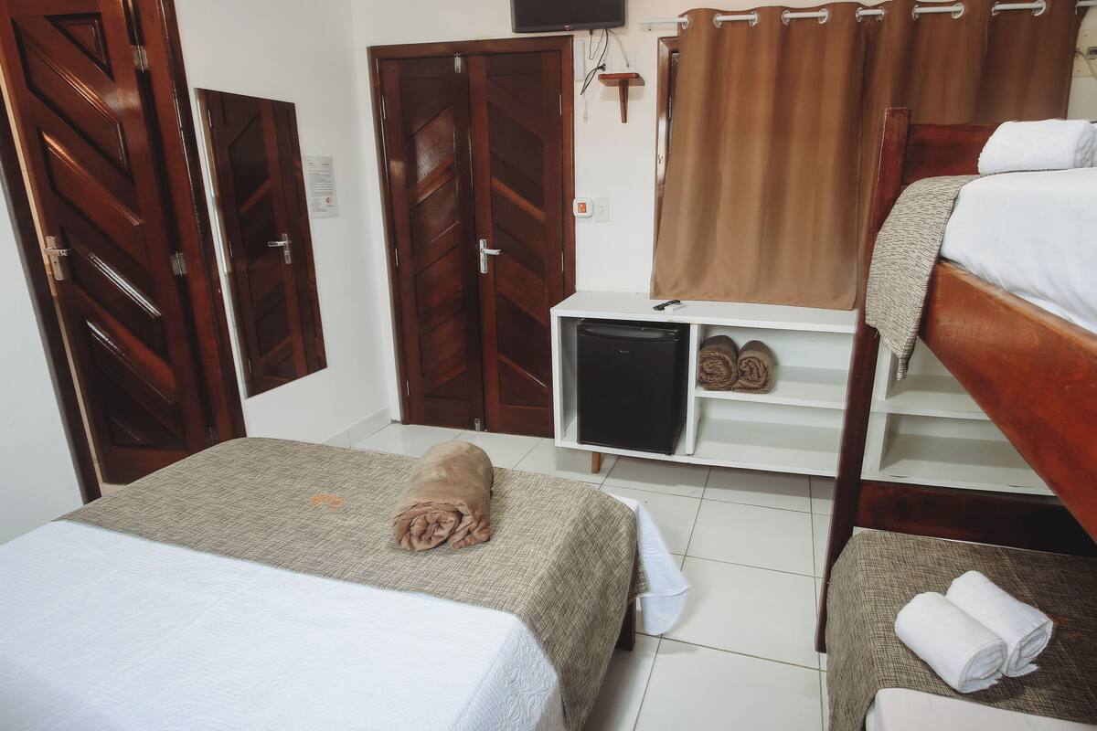 Una habitación pequeña y ordenada con dos camas, un refrigerador pequeño y una repisa con zapatos y una toalla.