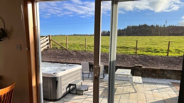 Een terras met een hottub, zitplaatsen buiten en uitzicht op een groen veld.