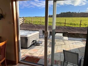 Eine Terrassenfläche mit Whirlpool, Sitzgelegenheiten im Freien und Blick auf ein grünes Feld.