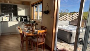 Een eetgedeelte met een houten tafel en stoelen, een keuken met witte kasten en een zwarte spatwand, en een zichtbare jacuzzi door een glazen deur.