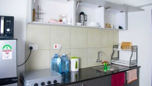 Cozinha compacta com geladeira, fogão e pia. Há garrafas de água, uma cafeteira e um escorredor de louça no balcão.