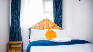 Cama bem arrumada com cabeceira de madeira, colcha azul e travesseiro branco com detalhe laranja.