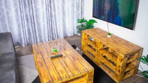 Uma sala de estar com uma mesa de centro de madeira, uma televisão na parede e um sofá cinza.
