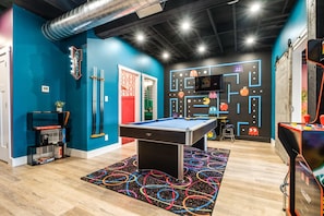 A pool table in a room with blue walls, a neon sign, and a wall with arcade game graphics.