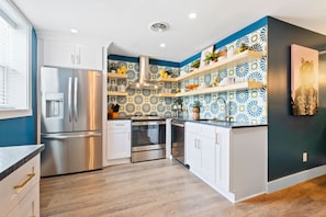 A modern kitchen with stainless steel appliances, white cabinetry, and decorative blue and white tiles.