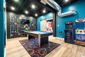 A pool table with a colorful circular rug, arcade games, and a wall with a maze design.