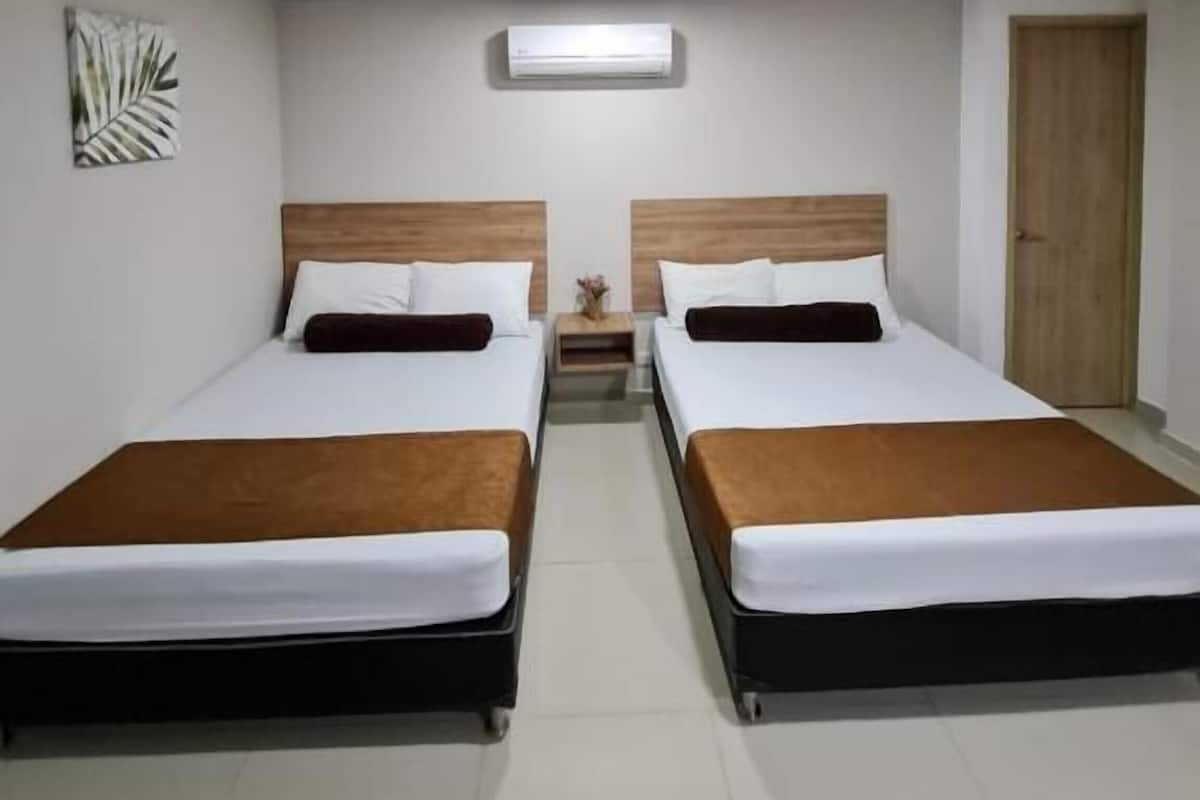 A hotel room with two beds, a ceiling light, a door, and a wall art piece.