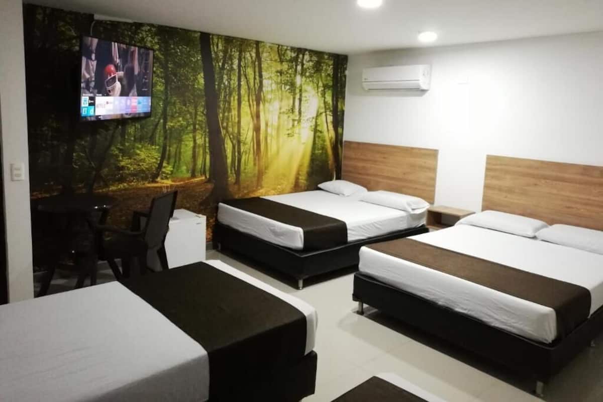 A hotel room with two beds, a TV, and a forest-themed wall mural.