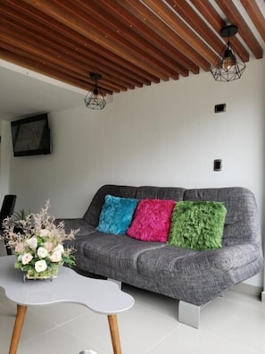 Una sala de estar moderna con un sofá gris, cojines coloridos, una mesa de centro blanca y techo de madera.