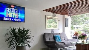 A modern living room with a flat-screen TV displaying 'GREATEST HITS 80's-90's', a grey sofa, a coffee table, and a potted plant. - HOTEL SURAMERICANA (Medellín)