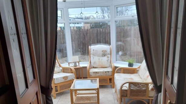 Une véranda meublée de mobilier en osier, dotée d’un ventilateur de plafond et offrant une vue sur le jardin arrière.