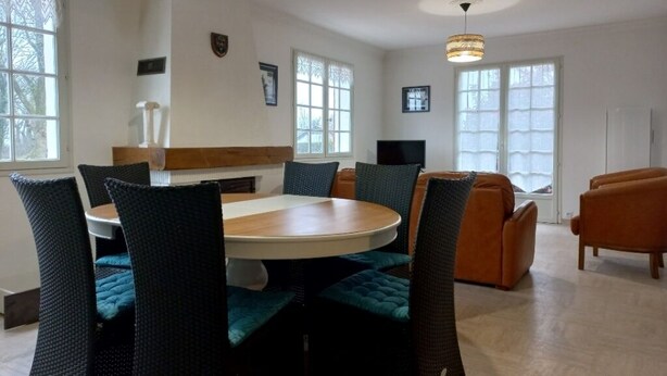 A dining area with a round table, chairs, and a sofa. There are windows with curtains, a television, and a coat rack. - 12 km St Gilles Croix de Vie to Coex. Sea, Golf, 3 lakes. 25 km Sables d'olonne  (Coëx)