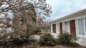 A building with a white facade and red shutters, surrounded by trees with pinkish buds. - 12 km St Gilles Croix de Vie to Coex. Sea, Golf, 3 lakes. 25 km Sables d'olonne  (Coëx)