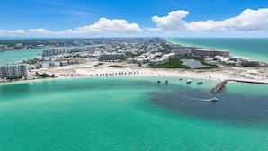 Vue aérienne d’une station balnéaire avec une plage, des eaux turquoise et limpides, et un port de plaisance.