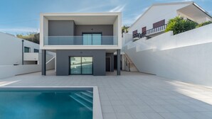 Una casa moderna de dos pisos con piscina, un balcón y una escalera que lleva al piso superior.