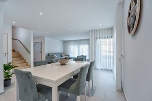 A modern living room with a staircase, a dining area with a white table and grey chairs, and a large wall clock. - Villa Foz - Holiday Villa with Private Pool By SCH (Foz do Arelho)