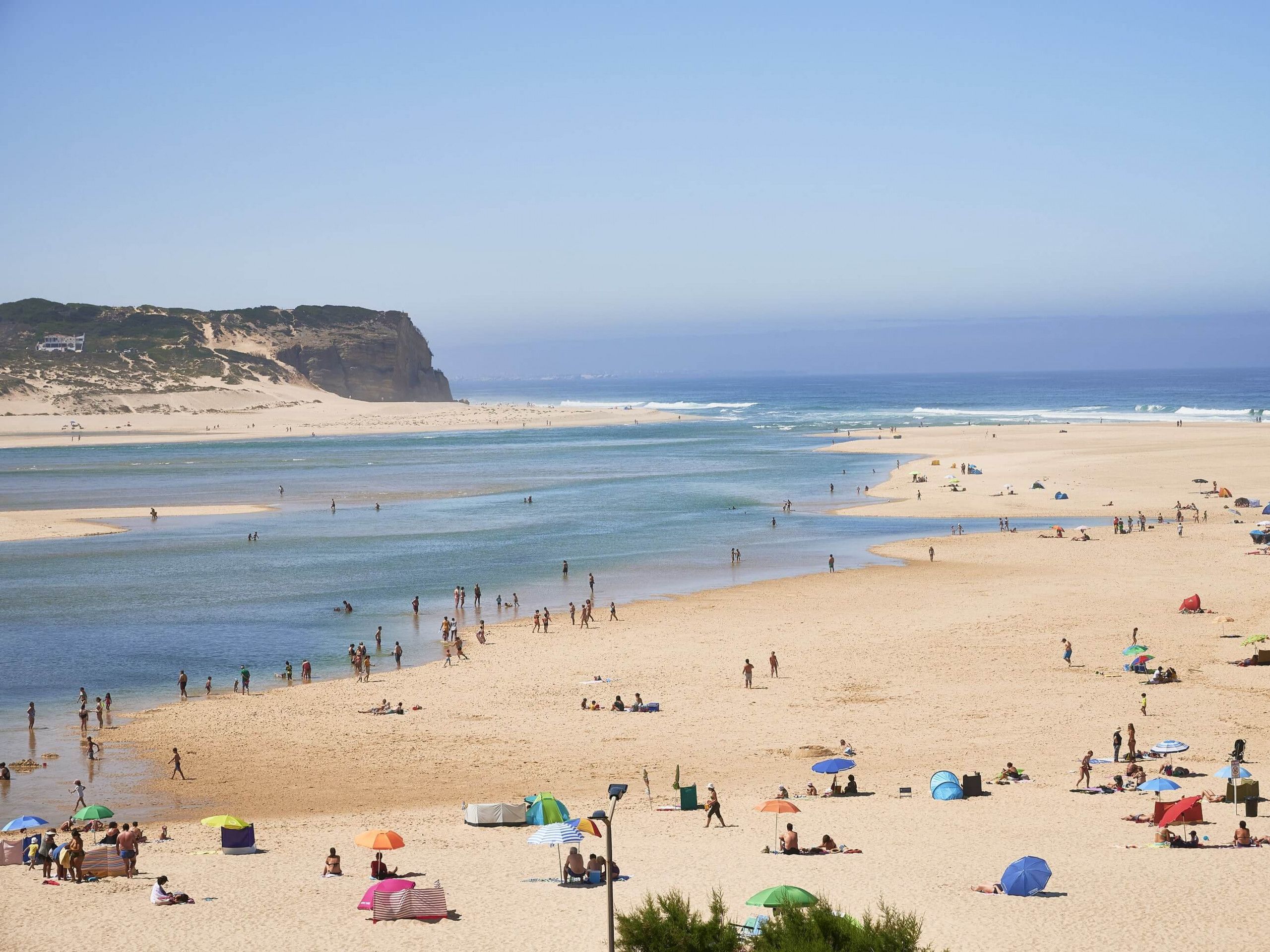 Una playa con tiendas de campaña y sombrillas, una orilla arenosa y un acantilado al fondo.
